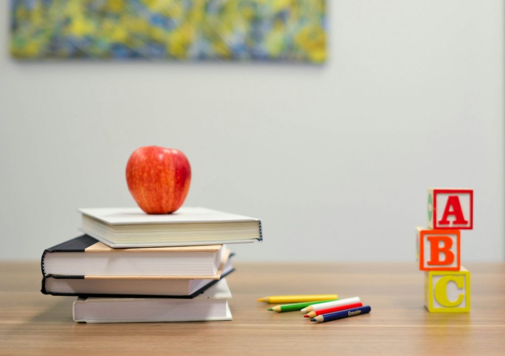 books stacked on table with apple on top and other school supplies.